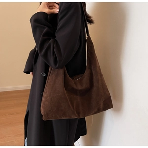 Détail d'un grand sac hobo en daim marron foncé porté dans un studio au style minimaliste