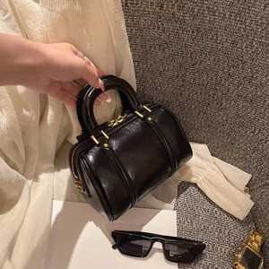 Glossy black Boston handbag with gold zippers on a grey sofa, retro shoulder bag style