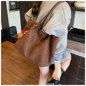 Detail of a large brown suede tote bag with stylish pom-pom charms for autumn and winter