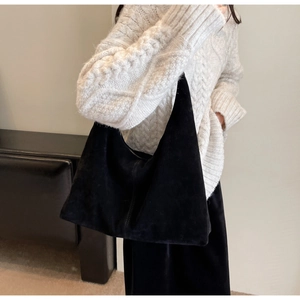 Détail d'un sac hobo noir texturé porté par un mannequin dans un décor minimaliste