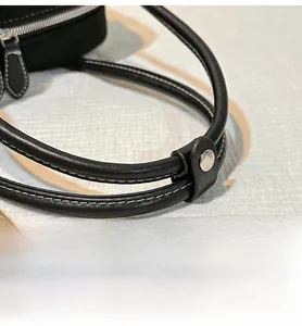 Detail of black leather bag handles with white stitching and silver metal buckle