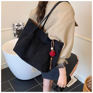 Detail showing the matte black tote bag with red pompom charm and thin shoulder straps