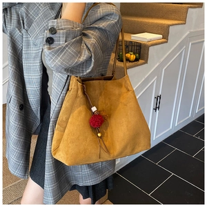 Detail of tan suede tote bag with decorative red pom-pom charm for daily commute