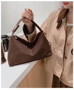 Detail of dark brown suede handbag with golden hardware held by model in trench coat