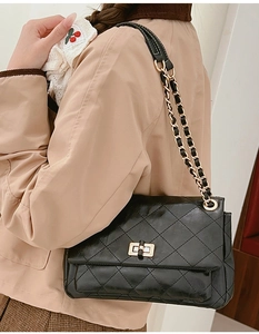 Detail of black quilted leather shoulder bag with gold clasp and metal chain strap