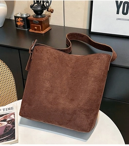 Close-up of large brown suede hobo bag with wide shoulder strap on white table
