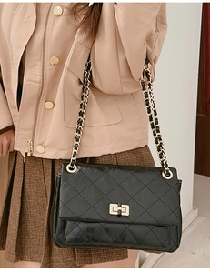 Detail of black quilted shoulder bag with gold chain strap and rectangular turn-lock closure