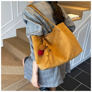 Detail of a large suede tote bag in camel yellow with pompom and tassel decorations