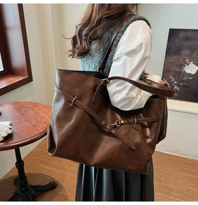 Detail view of large dark brown tote bag with buckle straps and metal eyelets on model