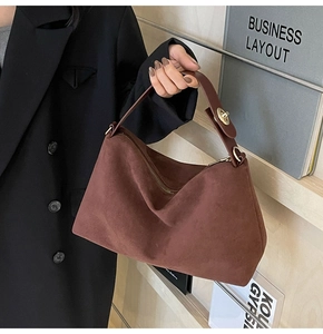 Close-up of brown suede handbag featuring wide top handle and gold metal ring detail