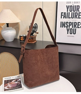 Detail of dark brown suede bucket bag with adjustable strap in a retro lifestyle setting