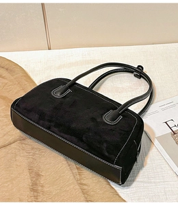 Detail of black suede shoulder bag with contrast white stitching and minimalist aesthetic