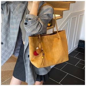 Detailed close-up of brown suede tote bag with decorative fur ball and wood bead charm