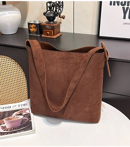 Detailed view of large brown suede tote bag with textured finish on white table