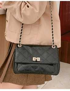Detail of black quilted leather shoulder bag with gold chain strap and twist-lock buckle