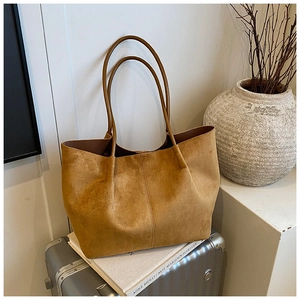 Close-up of brown suede tote bag on a suitcase showing fine stitching and soft texture