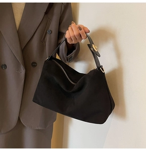 Detailed view of matte black suede handbag with gold zipper and metal buckle accents