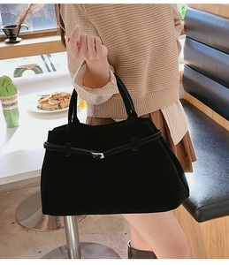 Détail d'un sac cabas en daim noir avec boucle argentée tenu par un mannequin