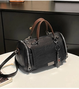 Dettaglio della borsa Boston nera con trama in pelle martellata, manici marroni e charm