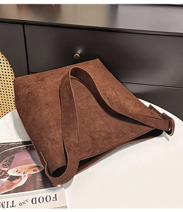 Detail of a large dark brown suede tote bag on a white table in a cozy home setting