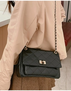 Classic black quilted shoulder bag with gold chain strap worn over a beige trench coat