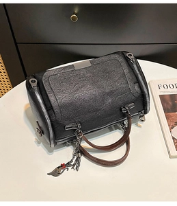 Dettaglio borsa Boston con cerniere argento, manici marroni e ciondolo gatto su base bianca