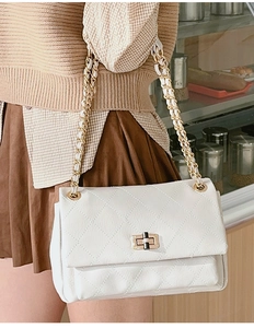 Close-up of white quilted faux leather shoulder bag with golden chain and metal lock