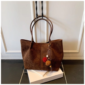 Detail of a large dark brown suede tote bag with a decorative tassel charm on a strap
