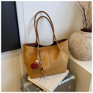 Detail of tan suede tote bag with boho charm on a white book and silver suitcase