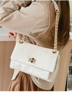 Close-up of a white quilted chain bag with a gold metal twist lock on a shoulder strap