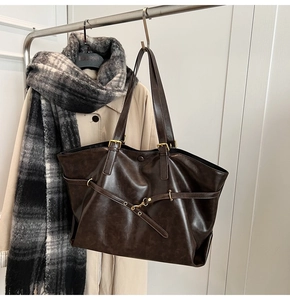 Detail of a large brown tote bag with metal buckle on a beige trench coat background