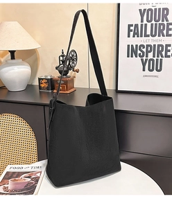 Minimalist black suede tote bag with slim shoulder strap on a clean white table setup