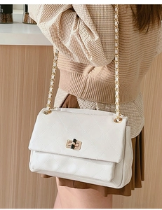 Close-up of a white quilted crossbody bag with a bamboo-style gold twist lock and chain