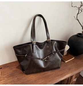Detailed close-up of dark brown leather tote bag with gold ring and buckle on wooden bench