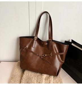 Detail of dark brown leather tote bag with decorative buckle and eyelet strap accents