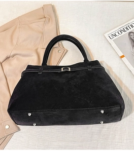 Détail d'un sac cabas en daim noir avec boucle argentée et pieds de protection