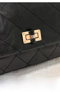 Detail shot of black quilted leather with golden square swivel lock on a crossbody bag