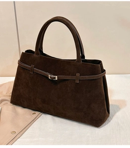 Détail d'un sac cabas en daim marron foncé avec boucle en métal rétro et texture mate