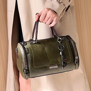 Borsa Boston vintage verde con manici e portachiavi a gatto, abbinata a un trench classico