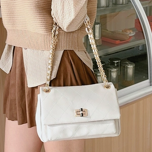 Quilted white chain crossbody bag with a metallic turn-lock displayed in a bakery setting