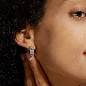 Macro shot of a model wearing a rainbow hoop earring with five rows of colored zircons
