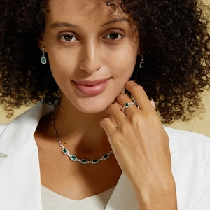Nahaufnahme eines Models mit Halskette, Ohrringen und Ring mit grünem Smaragdschliff
