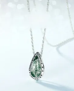 Macro shot of silver teardrop pendant with moss agate and intricate engraved patterns