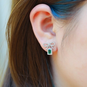 Boucles d'oreilles nœud en argent avec pierre émeraude et zircons portées par un modèle
