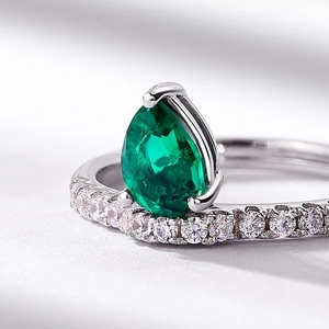 Pear-cut emerald ring in S925 silver with a micro-pave diamond band on white fabric