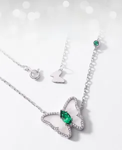 Macro shot of silver butterfly necklace featuring green emerald and white shell wings