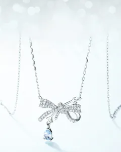 Detail of silver bow necklace featuring a light blue pear-cut gemstone and pavé stones