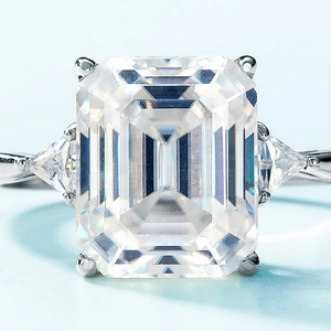 Emerald cut moissanite ring in S925 silver with trillion side stones on light blue background