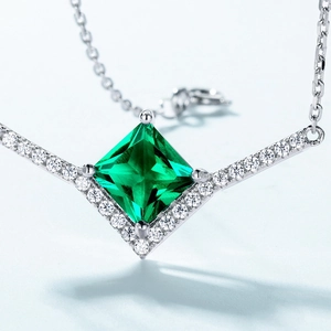 Princess cut emerald green pendant necklace with silver pavé halo on blue background