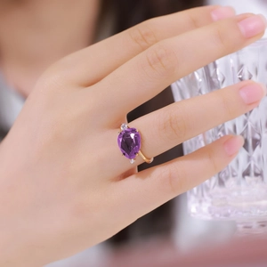 Detail of S925 silver ring with pear-cut purple crystal and gold setting on finger